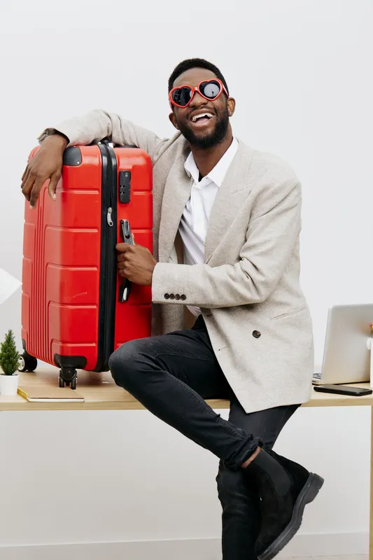 Smiling man with sunglasses and beard holding red suitcase in modern office setting. Casual style, cheerful expression, travel and business concept, vibrant colors, studio shot, lifestyle image, posit