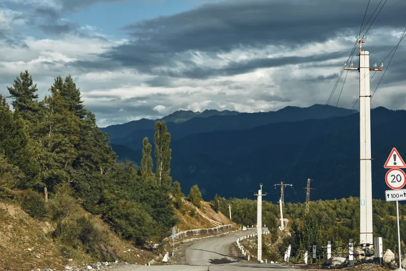 mountain road landscape with powerline and forest under cloudy sky on a rural asphalt curve, poles and signs, nature scene for travel and adventure authenticity inclusivity