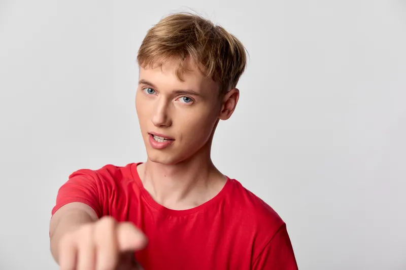 Man in a red shirt points at the camera with a confident direct gaze, a bold hand gesture producing an engaging stock image for marketing, tutorials and social content.