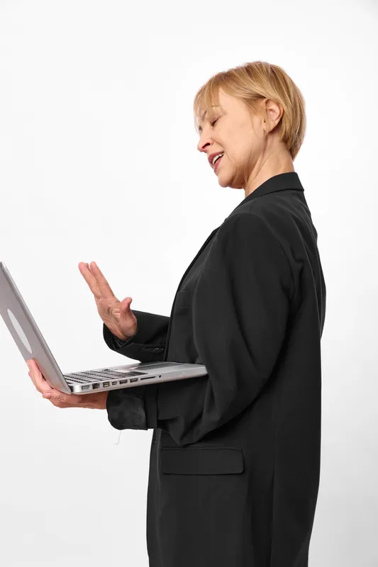 Woman in black suit using laptop in office profile, with smile and waving hand on white background, conveying technology and professional business communication, lighting