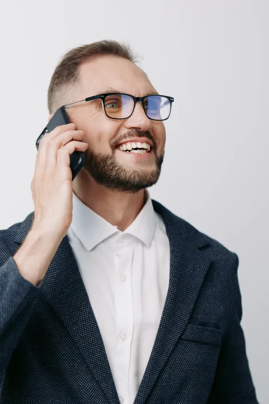 Professional businessman on a call, smiling warmly and confidently, conveying friendly emotion and approachability against a solid colored background suitable for corporate use.