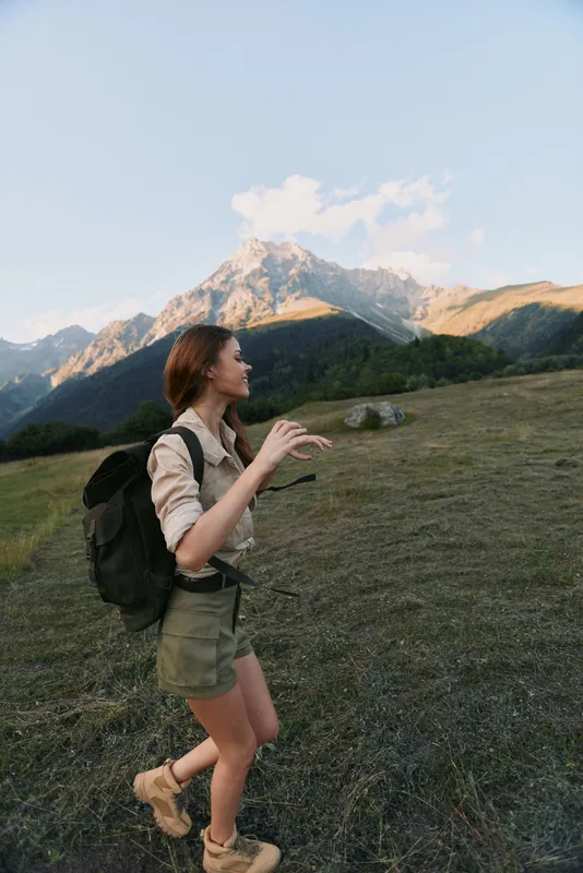 Cheerful woman hiking outdoors, backpack on, sunlit mountain meadow, enjoying nature and fresh breeze, relaxed posture, candid moment, vibrant colors, outdoor lifestyle