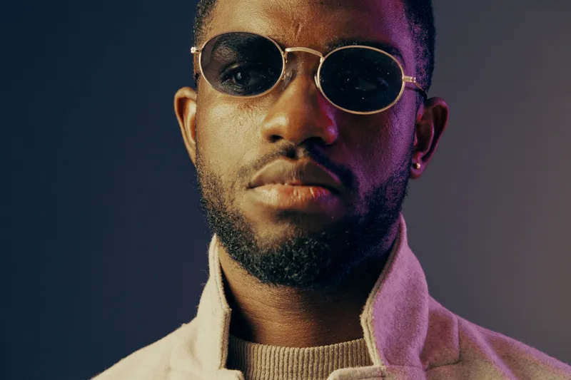 Confident young man with stylish sunglasses and a fashionable coat, showcasing warmth and style against a colorful gradient background