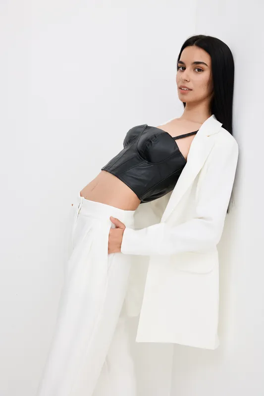 stylish woman wearing black leather corset and white suit leaning back against white wall, with long straight hair and calm expression in modern minimalistic style