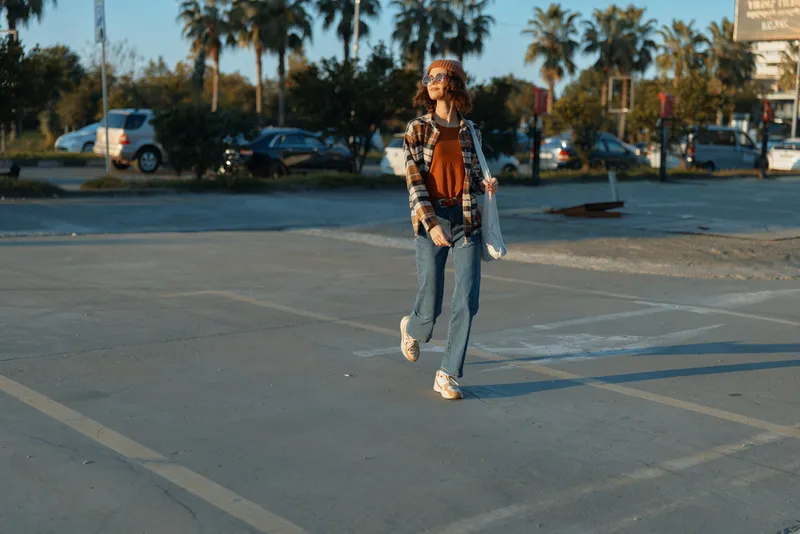 woman walking and smile across a sunlit parking lot with palm trees, candid lifestyle portrait capturing authenticity and golden hour glow, mindful living and emotional storytelling