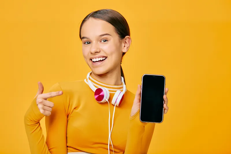 Fitness-minded woman in a bright orange workout top holds a smartphone and headphones against a vibrant orange backdrop, highlighting healthy living, digital fitness tools and motivation.