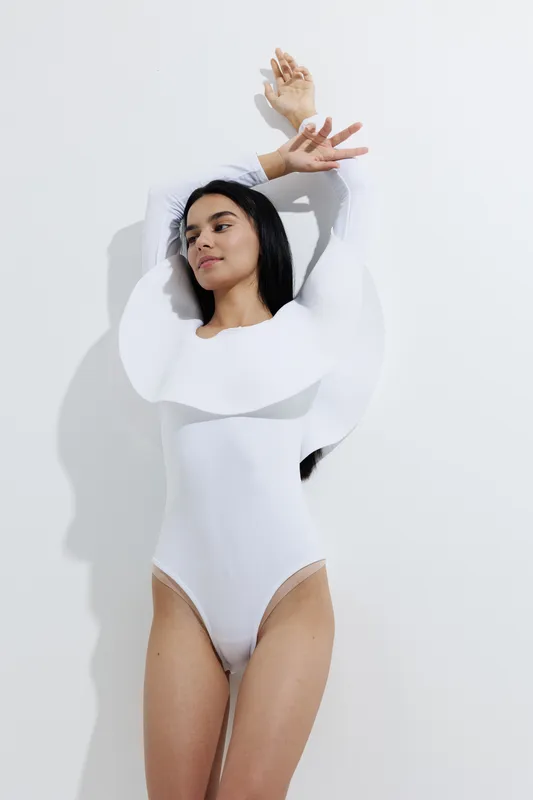 Woman sport fitness portrait in white bodysuit with dynamic pose and natural lighting, showcasing healthy lifestyle and elegance in minimalistic studio setting.