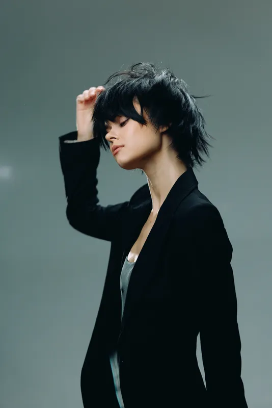 Young woman with short black hair in black jacket posing with closed eyes in studio, expressing calm and confidence.