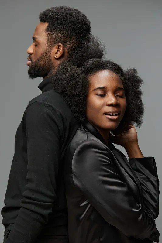 A stylish couple with natural textured hair pose back to back, showcasing confidence and intimacy in a modern studio setting with a neutral background