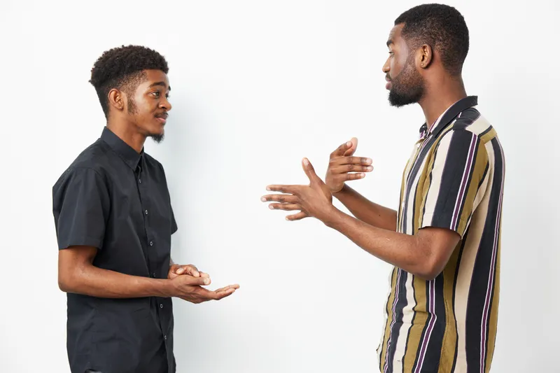 Engaging conversation between two African American men, showcasing friendship and connection through expressive body language and smiles in a bright background.