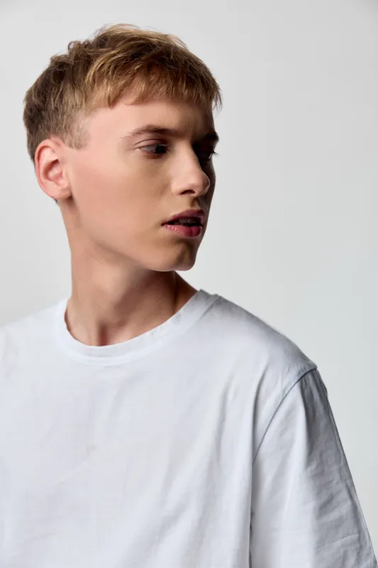 Young man in white shirt in a studio, fashion oriented scene with calm side view, minimal lighting, casual mood suitable for lifestyle and contemporary photography projects