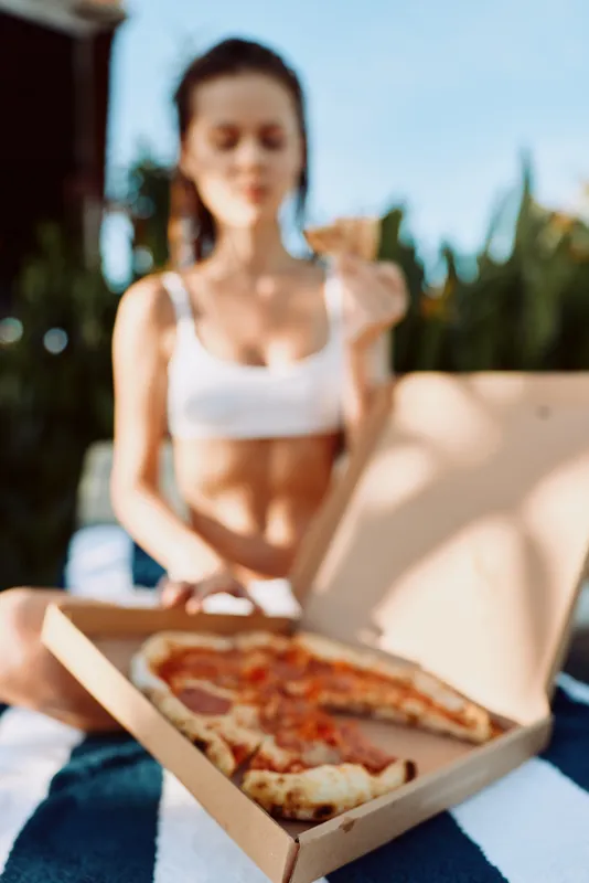 A pizza loving woman enjoys outdoor lunch, casual lifestyle, sunlit garden setting, and a relaxed mood while opening a pizza box, capturing a candid moment of simple dining and fresh aroma.