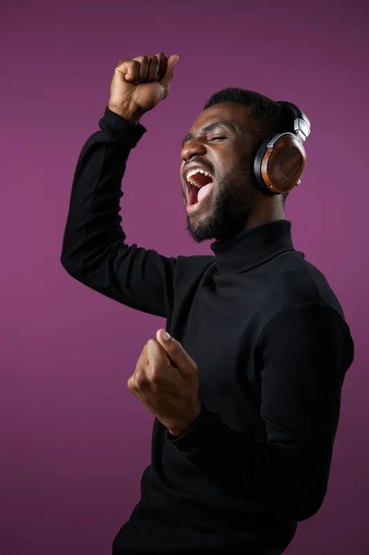 Joyful Black man dancing with headphones on a purple background, expressing excitement and happiness through music and movement