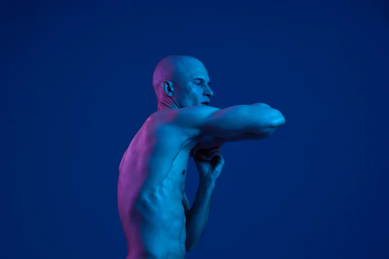 A male posing dynamically against a blue background, showcasing strength and grace. The image captures an artistic dance movement in a vibrant, colorful style.