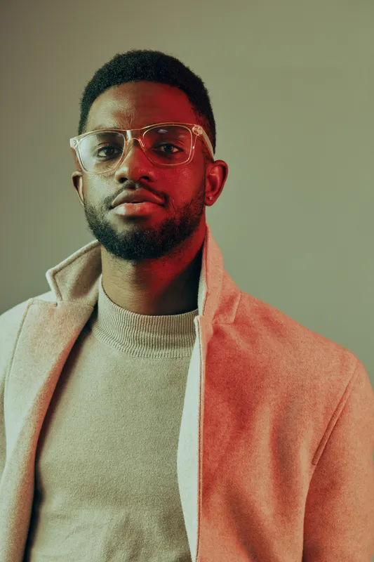 Stylish young Black man wearing glasses and a fashionable sweater poses confidently against a gradient background, showcasing modern men s fashion and personal style