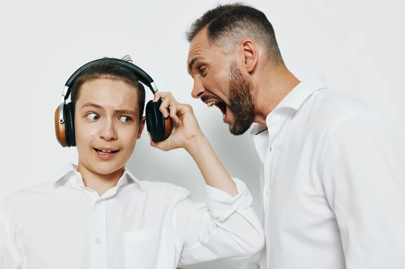 A business professional man shows strong emotion as he leans toward a younger colleague wearing headphones, against an isolated colored background, creating a dynamic office moment of leadership and