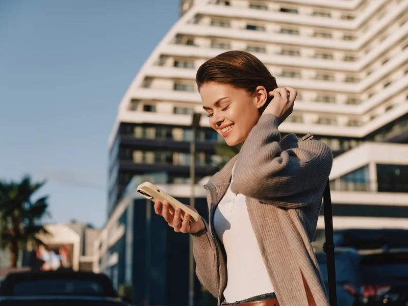 A cheerful business professional is seen texting in a modern urban environment. She smiles and appears engaged, creating a positive and dynamic business atmosphere.