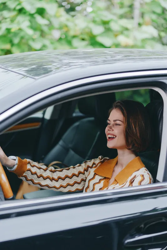 A joyful woman enjoys driving in a sleek car, smiling as she sits behind the wheel, radiating confidence, freedom, and a relaxed everyday moment.