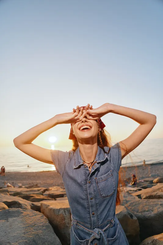 lifestyle woman enjoying sunset in modern boho-western denim dress at beach with film color warm tones and relaxed street style vibe