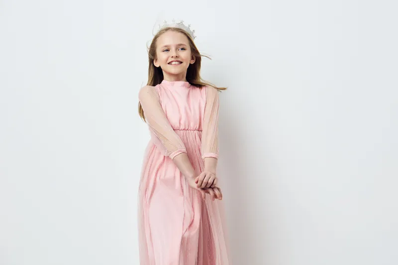 A smiling girl in a pink dress with delicate sleeves, showcasing joy and innocence against a light background, perfect for children s fashion and celebrations