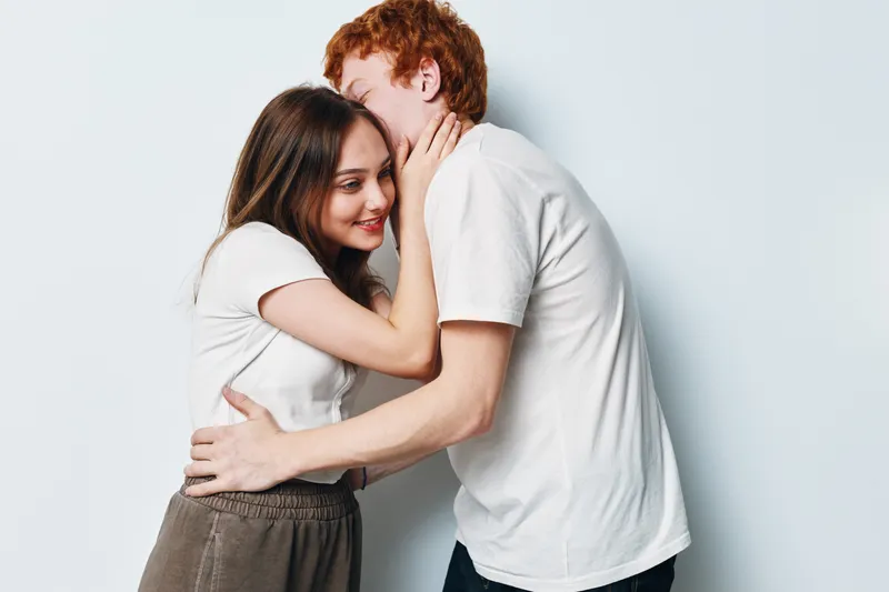Couple embracing with affection and intimacy on white background. Young man and woman touching faces, showing love, connection, and care in casual clothes, relationship moment.