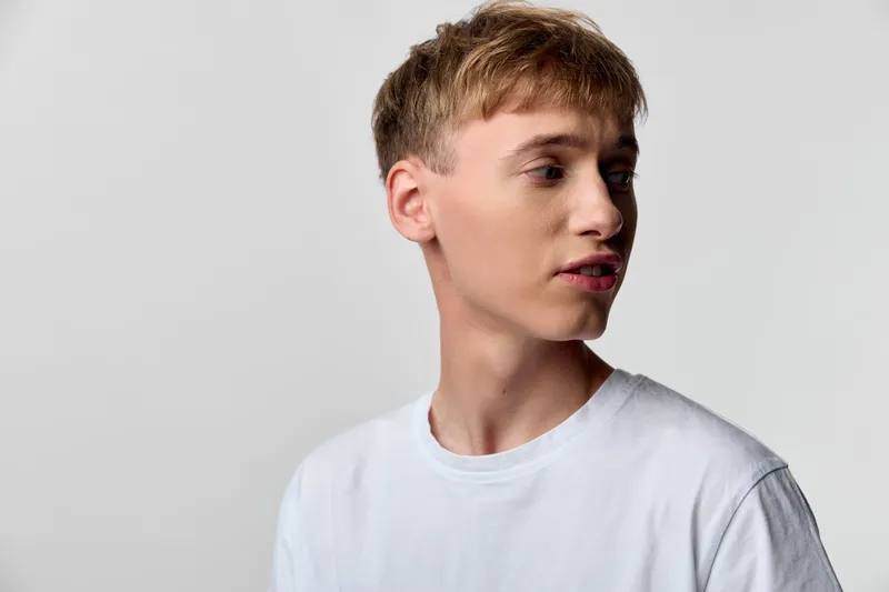 Young man in a plain white tshirt turns his head in a clean studio setting, showcasing casual style, natural lighting, and a candid moment with a thoughtful expression.