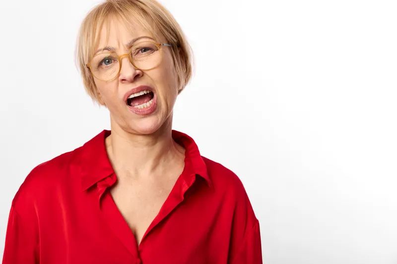 Woman with glasses, blond short hair, surprised expression, red shirt portrait on white background, studio closeup, speaking with open mouth, direct gaze, neutral light, copy space