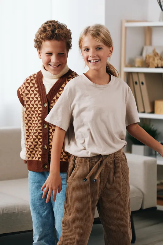 Two cheerful children pose in a cozy home setting, showcasing authenticity, school theme, and lifestyle with natural smiles and relaxed style.