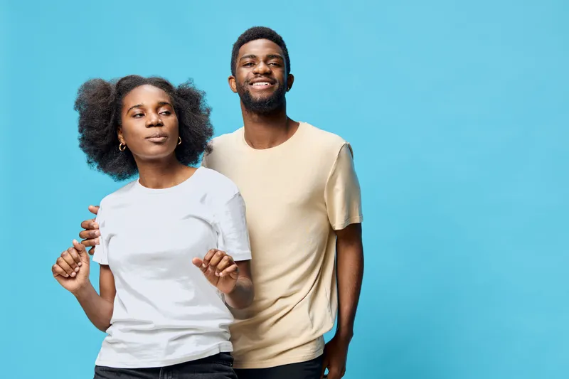 Young African couple smiling joyfully against a blue background, wearing casual outfits, showcasing their connection and happiness in a vibrant, modern style