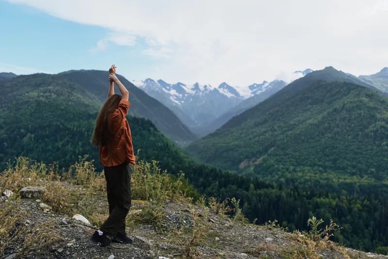 A hiker stands on a rocky ridge amid mountains, gazing toward a vast landscape, enjoying nature and outdoors, a moment of freedom and adventure in scenic alpine scenery