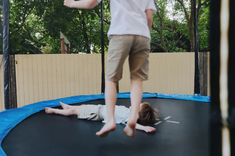Two children joyfully playing on a trampoline, showcasing fun, laughter, and carefree moments in a vibrant outdoor setting filled with greenery.