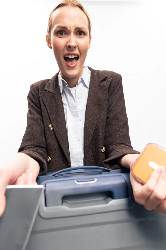 Surprised young woman in brown jacket holds toolboxes in hands, looks shocked on white background. Concept of repair, construction, tools, and unexpected situations with equipment.