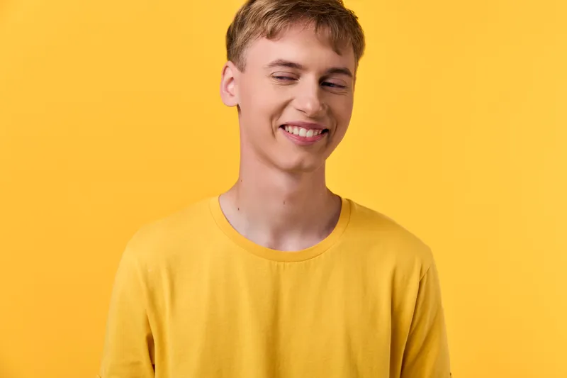 Close up of a smiling youth in a yellow shirt against a bright yellow background, showcasing cheerful energy, casual style, confident expression, vibrant fashion for lifestyle and branding photography