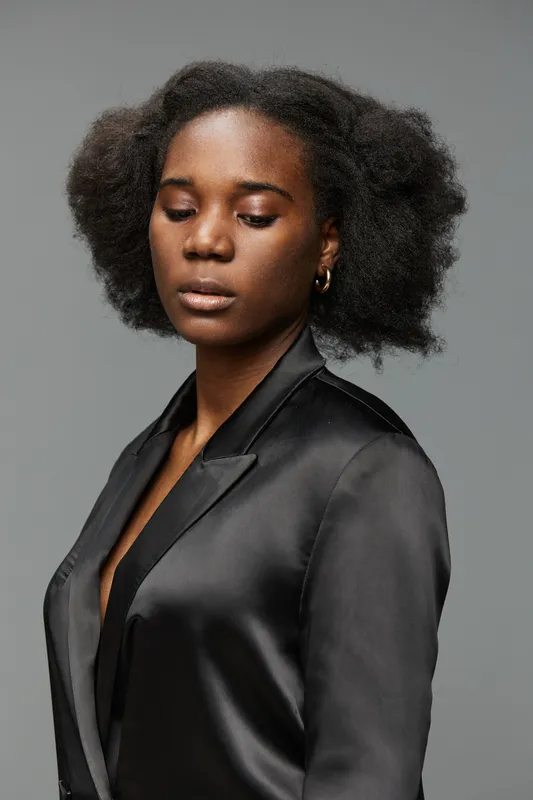 Elegant portrait of a confident Black woman with natural hair, wearing a sleek black outfit, showcasing calm emotions against a gray background