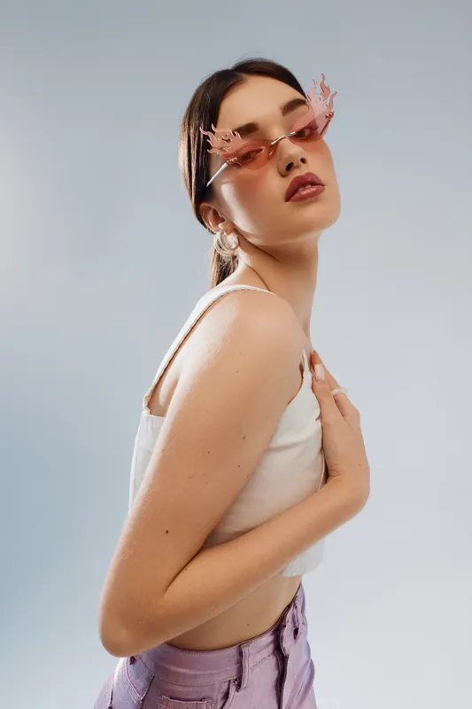 Young woman in stylish pink sunglasses and white top poses confidently against a neutral background. Concept of beauty, fashion, and modern accessories with soft lighting.