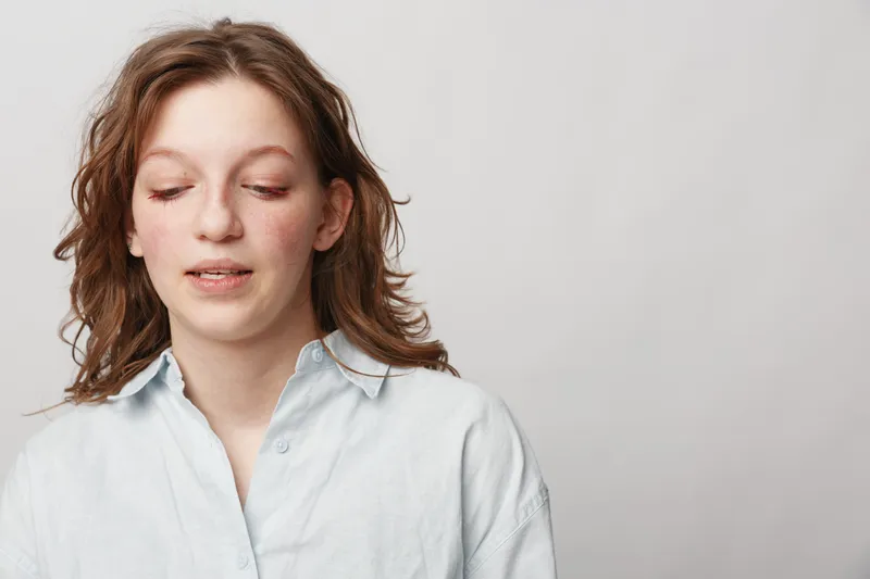 Young woman with closed eyes and relaxed expression wears white shirt against plain background. Concept of calm, introspection, natural beauty, and peaceful moment in studio portrait.