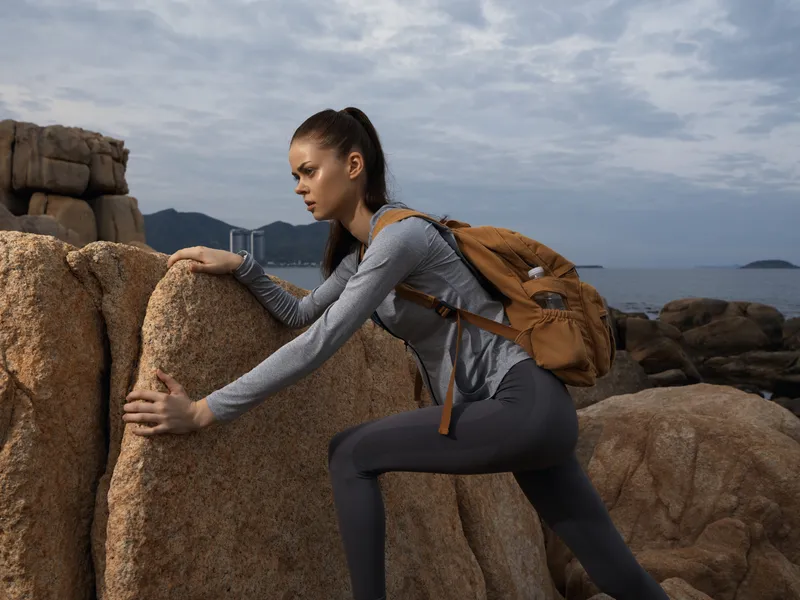 Young woman climbing rocks in activewear, emphasizing fitness and adventure in a scenic coastal background, perfect for outdoor and sports concepts