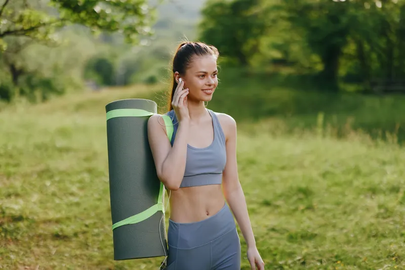 Fit young woman carrying a yoga mat in nature, showcasing a healthy lifestyle, relaxation, and outdoor fitness during summer
