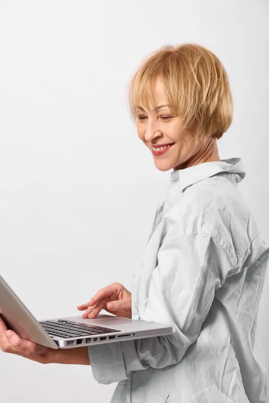 Smiling woman with short hair, using laptop indoors, remote office work, technology and communication focus, clean neutral background with soft light, modern casual style