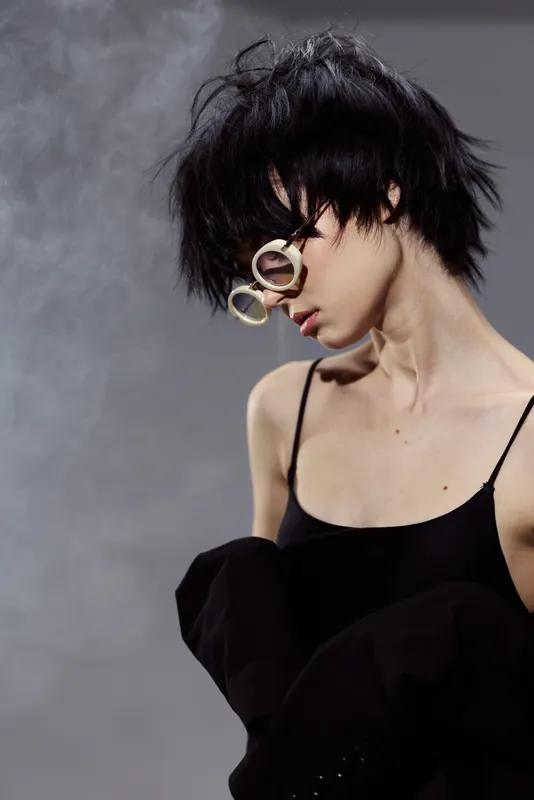 Stylish young woman with short black hair wearing glasses and a black top in a smoky atmosphere