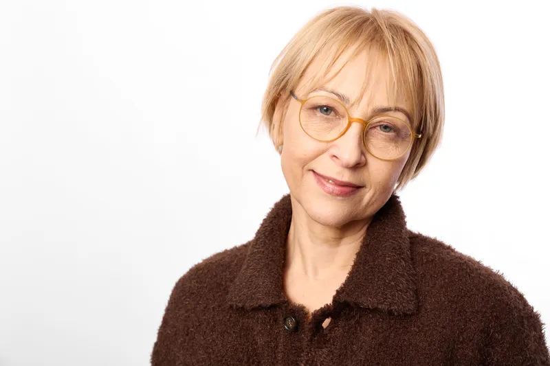 Elderly woman portrait, glasses, smiling face, short blond hair, warm expression, closeup on white background, calm neutral mood, studio lighting, soft focus, high key