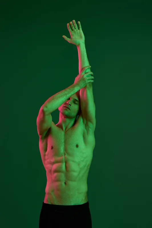 Athletic man stretching against a green background, showcasing toned muscles and healthy lifestyle. This energetic pose evokes vitality and movement in a vibrant setting.