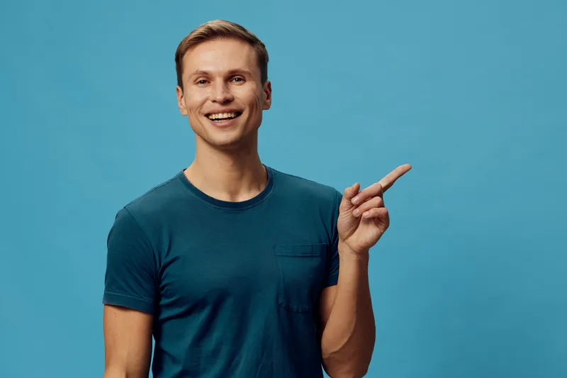 smiling man pointing index finger wearing casual blue t-shirt isolated on teal background digital nomad concept