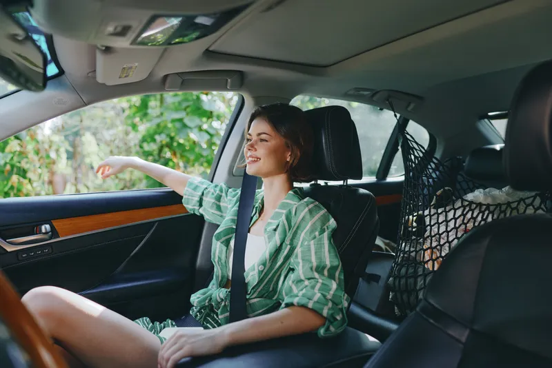 A young woman drives a car in a relaxed setting, wearing a green striped shirt and a safety belt.