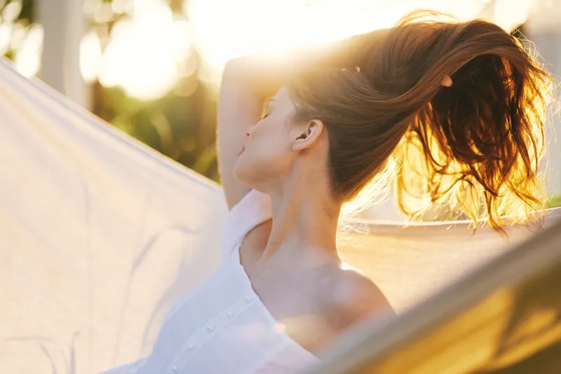 A serene woman with flowing hair enjoying the golden sunlight, embodying tranquility and elegance in a summer setting, perfect for healthy lifestyle imagery