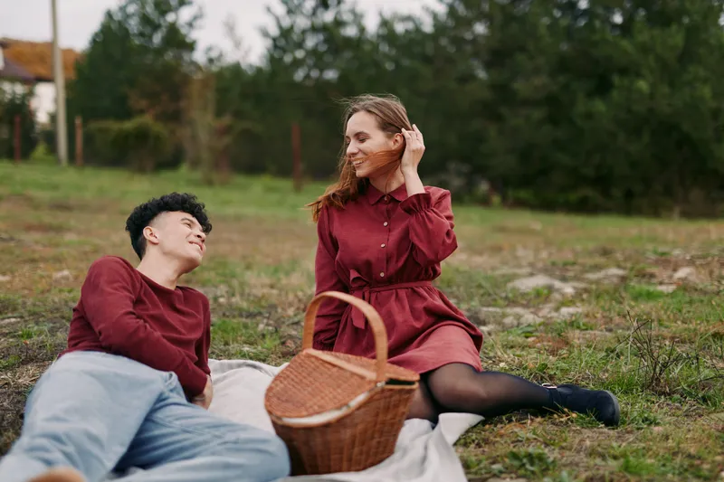 Candid outdoor picnic portrait of a young couple sharing a genuine moment on a blanket, natural expressions and composition emphasizing authenticity and credibility in daily life.
