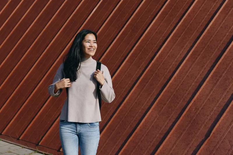 woman, backpack, casual, smiling, outdoor, urban, wall, fashion, travel, lifestyle, is captured beside a diagonal wooden wall in an urban setting, showcasing a relaxed look and confident vibe