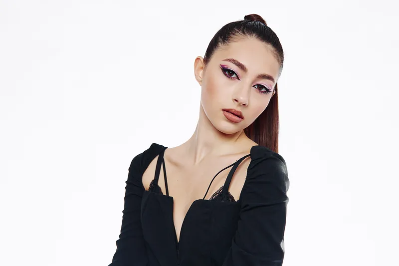 Stylish young woman poses in black fashion outfit with bold makeup and flawless skin. Creative beauty portrait on white background. Concept for fashion, glamour, and modern style.