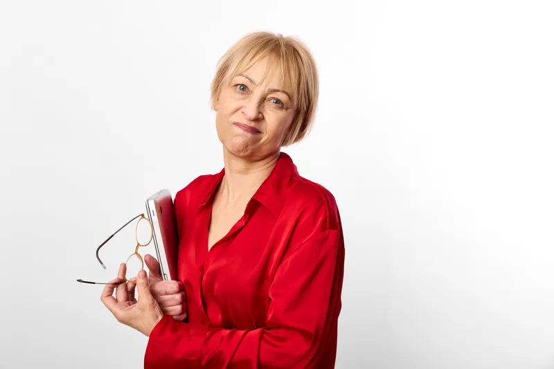 Senior woman in red blouse holding eyeglasses, studio portrait on white background, looking at camera, confident mood, soft even lighting, calm warmth