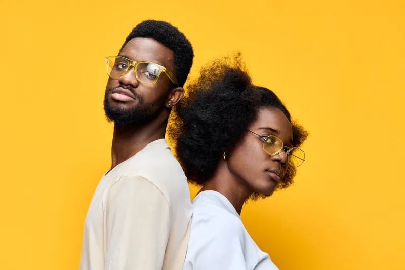Young couple with stylish glasses posing against a bright yellow background, showcasing modern fashion and confidence in a vibrant, youthful atmosphere